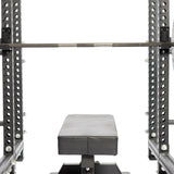 A flat weight bench sits under a racked barbell in a power rack outfitted with Bells of Steel Standard J-Cups, which have UHMW protection and multiple adjustment holes and markings.