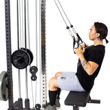 A person with medium-length hair and a tattoo on their left arm uses the Bells of Steel Cable Tower’s adjustable handles for a seated row, pulling them toward their chest against a white background.
