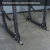 Close-up of the flat base feet of the Bells of Steel Manticore Flat Foot Power Rack - Prebuilt (3" x 3", 1" Holes) on a tiled floor, with text above reading, "Flat feet provide a solid and stable base." Perfect for any home gym setup.