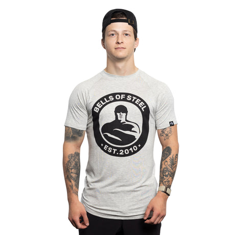 A man in a backward black cap and light gray Bells of Steel Bamboo T-Shirt stands facing forward, displaying tattooed arms, against a plain white background.