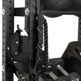 A close-up of the Bells of Steel Utility Hook on a gym rack, storing a black baseball cap, a black tricep rope attachment, weights, and a medicine ball for efficient gym organization.