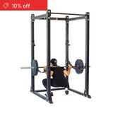 A person in black workout clothes and a cap does barbell squats inside the Bells of Steel Hydra Flat Foot Power Rack Builder (3" x 3", ⅝" Holes). A red banner says "10% off," ideal for upping your home gym game.