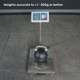 A digital scale sits on a gray tiled floor, displaying a weight as it holds a Bells of Steel Competition Kettlebell. The screen reads “Weights accurate to +/- 200g or better,” giving users confidence when consulting any kettlebell weight guide.
