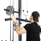 A person with tattoos on their left arm, wearing a black t-shirt and cap, performs a lat pulldown using the Bells of Steel Fat Bar - Lat Pulldown Bar, gripping it with both hands. Gym weights are loaded on the machine.
