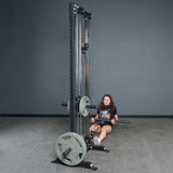 A woman uses the Bells of Steel Fat Bar - Lat Pulldown Bar on a cable machine in a gray-walled gym, performing seated rows to boost grip strength.