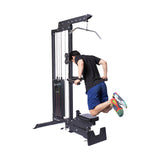 A man in a black shirt and blue shorts performs dips on the Bells of Steel Lat Pulldown Low Row Machine, using parallel bars with bent knees—highlighting this versatile home gym equipment for effective cable workouts.