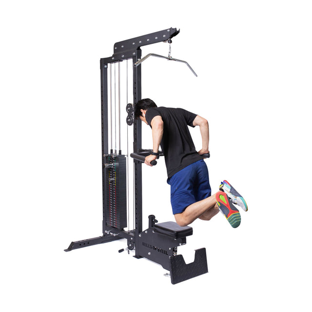 A man in a black shirt and blue shorts performs dips on the Bells of Steel Lat Pulldown Low Row Machine, using parallel bars with bent knees—highlighting this versatile home gym equipment for effective cable workouts.