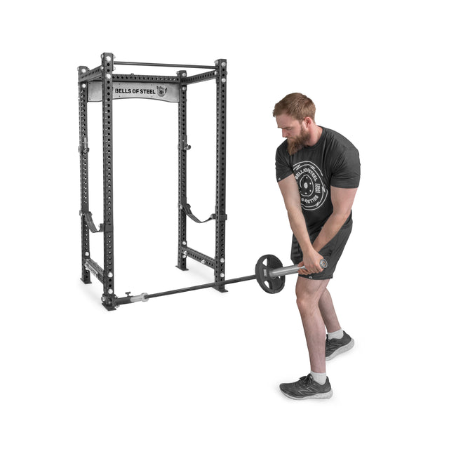 A man in athletic wear performs a strength workout, lifting a barbell from the UHMW-lined Landmine Rack Attachment by Bells of Steel, using both hands with unwavering focus.