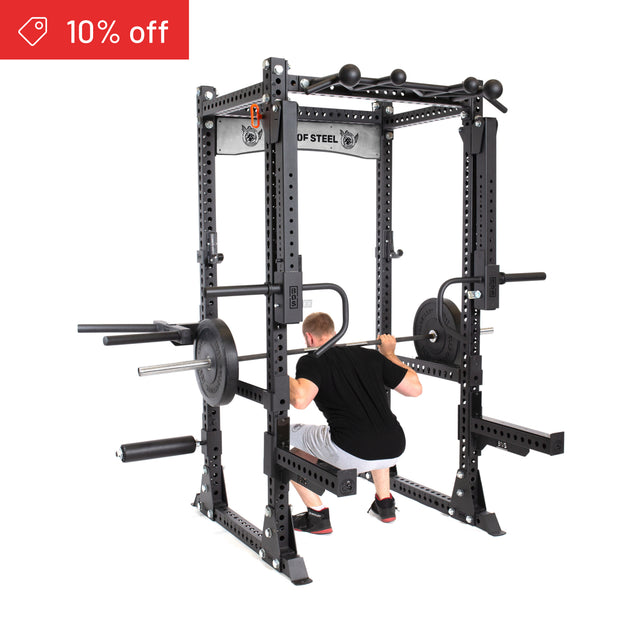 A man squats with a barbell inside the Bells of Steel Manticore Flat Foot Power Rack Builder (3" x 3", 1" holes), loaded with weight plates. A red "10% off" tag appears in the top left for your home gym upgrade.