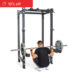 A man in black workout clothes performs a barbell squat inside the Bells of Steel Manticore Four Post Power Rack Builder, with a red "10% off" banner—perfect for any home gym.