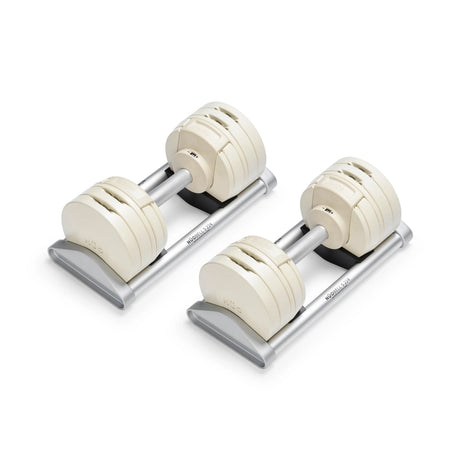The Bells of Steel NÜOBELL-S Adjustable Dumbbells, featuring cream-colored plates and silver handles, rest on matching stands—an ideal addition to your home gym.