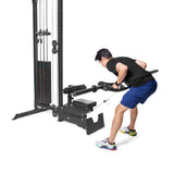 A person in blue shorts and a black shirt is using the seated row machine at the gym, gripping the handles. Their Arch Nemesis Swiss Bar by Bells of Steel becomes the weight stack looming in the background as they master their technique.