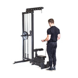 A person in black athletic wear stands beside the Bells of Steel Lat Pulldown Low Row Machine, holding the cable handle. This versatile black home gym equipment features a seat and footplate, displayed against a white background.