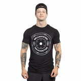 A man wearing a backward black cap and a Bells of Steel Bamboo T-Shirt with a weight plate graphic faces forward, smiling, with tattooed arms visible against a white background.