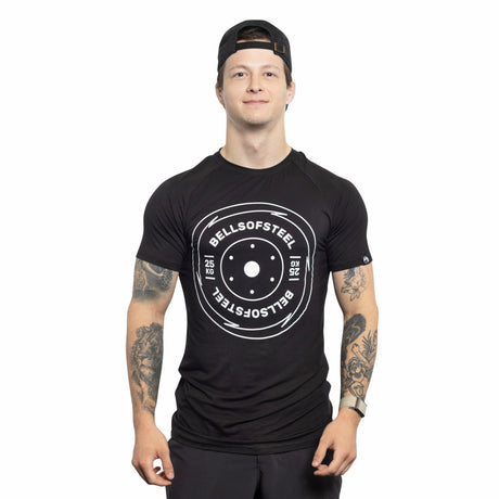 A man wearing a backward black cap and a Bells of Steel Bamboo T-Shirt with a weight plate graphic faces forward, smiling, with tattooed arms visible against a white background.