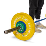 A person in black pants and checkered slip-ons admires a barbell with yellow Bells of Steel weight plates, secured by Spring Collars on its shiny chrome Olympic sleeves, set against a pristine white background.
