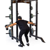 Wearing black athletic clothing and a cap, a person uses the Bells of Steel Seal Row Pad Rack Attachment to perform a bent-over reverse fly inside a power rack with weight plates on both sides.