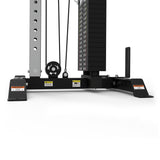 Close-up of the lower section of the Bells of Steel Cable Tower gym machine, featuring a weight stack, pulleys, cables, sturdy metal frame, adjustable handles, and warning labels. The equipment is shown against a white background.