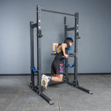 A person in athletic attire does a dip on parallel bars mounted to the Bells of Steel Hydra Half Rack - Prebuilt (3" x 3", ⅝" Holes) in a gym with gray walls and a tiled floor.