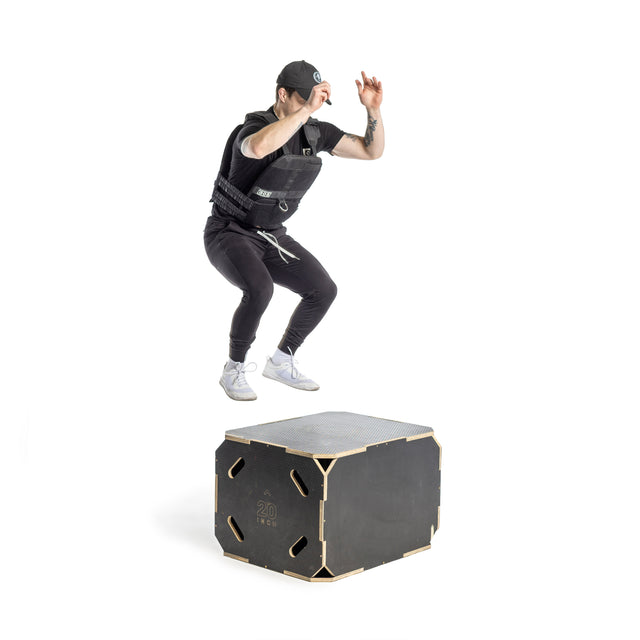 A person in athletic gear, including a cap and a Bells of Steel Weighted Vest, is captured mid-jump onto a black platform marked "20 18-24" in a brightly lit, white studio.