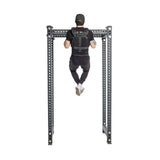 A man in a black cap and workout clothes performs a pull-up using a Bells of Steel Weighted Vest on a metal bar, showcasing his strength from behind with legs slightly bent, enhanced by the vest's adjustable training plates.